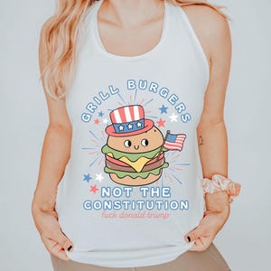 May include: White vest top featuring a cartoon burger wearing a patriotic hat and holding an American flag. The text reads "GRILL BURGERS NOT THE CONSTITUTION fuck donald trump" in blue and red.
