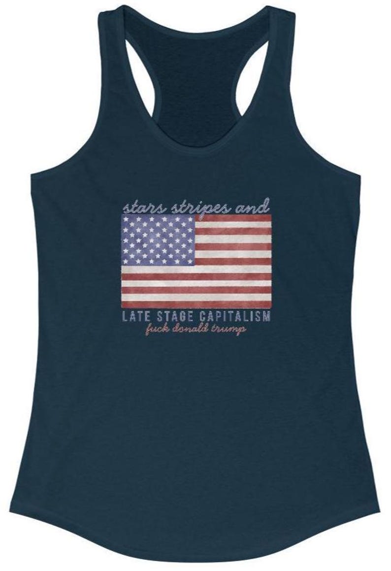 May include: Navy blue tank top with a racerback design. The front features a distressed American flag graphic with the text "stars stripes and" above and "LATE STAGE CAPITALISM fuck donald trump" below the flag.