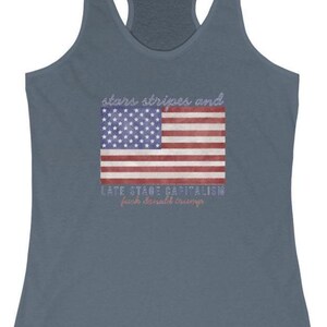 May include: A blue racerback tank top featuring an American flag design. The flag graphic includes the text "stars stripes and" above the flag and "LATE STAGE CAPITALISM from donald trump" below the flag.