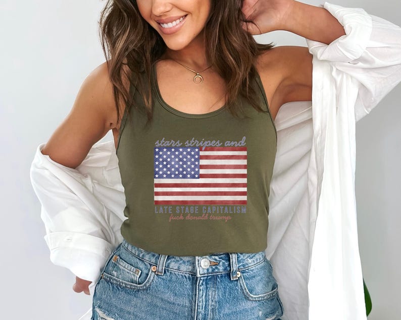 May include: Olive green tank top featuring an American flag design with the text "stars stripes and late stage capitalism fuck donald trump". The flag has red and white stripes and a blue field with white stars.