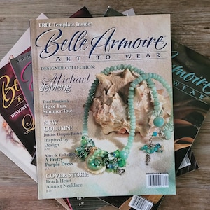 May include: A stack of Belle Armoire Art to Wear magazines with the top issue featuring a light green beaded necklace draped over a large seashell. The cover text includes Designer Collection Michael deMeng and Beach Heart Amulet Necklace.