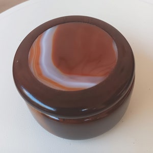 May include: A small, round wooden box with a lid. The lid is made of agate, with brown and white bands. The box is about 3 inches in diameter.