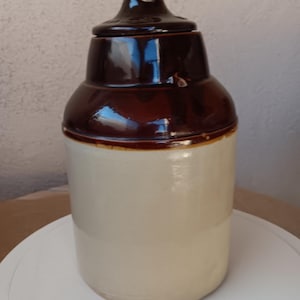 May include: A brown and white ceramic pitcher with a lid. The pitcher has a brown glaze on the top half and a white glaze on the bottom half.