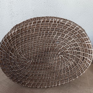 May include: A large, oval-shaped wicker basket with a woven pattern. The basket is made of natural brown wicker and has a smooth, even texture.