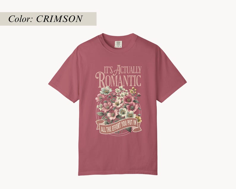 Pu&ograve; includere: T-shirt color cremisi con grafica floreale. La grafica include un bouquet di fiori rosa, bianchi e verdi, con la scritta "IT'S ACTUALLY ROMANTIC" sopra uno striscione con la scritta "ALL THE EFFORT YOU PUT IN."