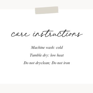 Pu&ograve; includere: Una scheda bianca con le parole "care instructions" in elegante scrittura. Sotto, elenca i dettagli di cura: lavare in lavatrice a freddo, asciugare in asciugatrice a bassa temperatura, non lavare a secco e non stirare. Un pezzo di nastro adesivo &egrave; in alto.