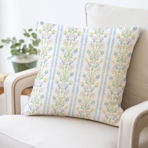May include: A white throw pillow with a floral pattern in shades of blue, pink, and yellow. The floral pattern is a repeating design of vertical stripes with small flowers and leaves.