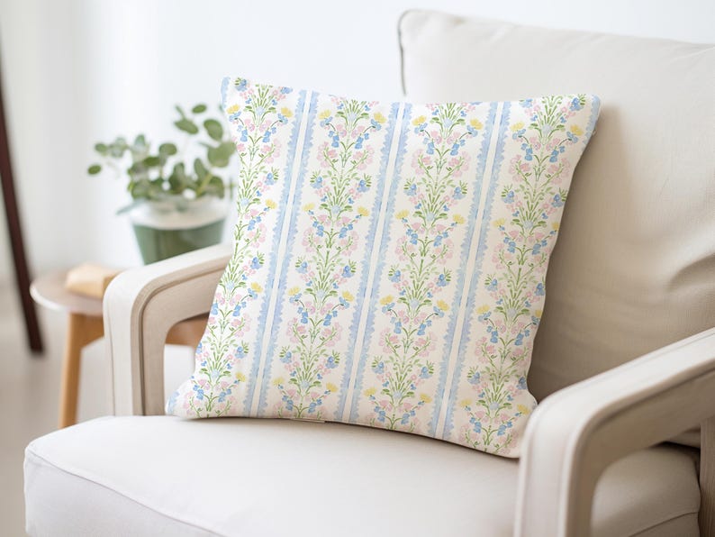 May include: A white throw pillow with a floral pattern in shades of blue, pink, and yellow. The floral pattern is a repeating design of vertical stripes with small flowers and leaves.