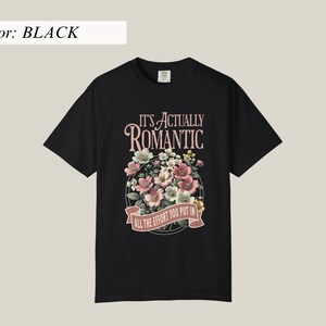 Pu&ograve; includere: T-shirt nero con un design floreale e la scritta "IT'S ACTUALLY ROMANTIC, ALL THE EFFORT YOU PUT IN". Il design presenta fiori rosa, bianchi e verdi in una disposizione circolare.