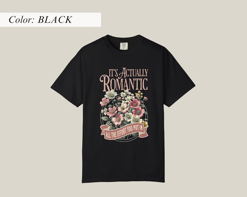 Pu&ograve; includere: T-shirt nero con un design floreale e la scritta "IT'S ACTUALLY ROMANTIC, ALL THE EFFORT YOU PUT IN". Il design presenta fiori rosa, bianchi e verdi in una disposizione circolare.