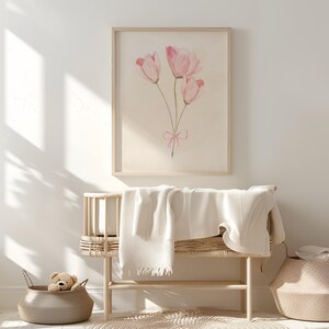 May include: A framed watercolour painting of three pink tulips with a pink ribbon tied around the stems. The painting is hanging on a white wall above a wicker bench with a white blanket.