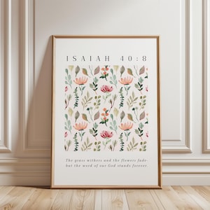May include: A printable wall art design featuring a floral pattern with pink and green watercolor flowers and leaves. The text "ISAIAH 40:8" and the quote "The grass withers and the flowers fade- but the word of our God stands forever." are printed in black text.