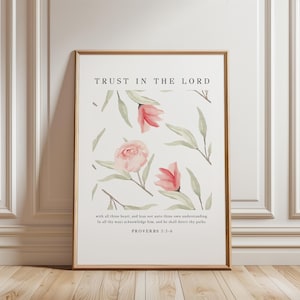 May include: A framed art print featuring the text "TRUST IN THE LORD" above a floral design. The artwork includes pink and red flowers with green leaves on a white background. The bottom of the print contains a Bible verse.