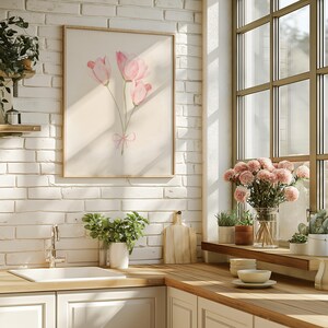 May include: A framed watercolour painting of pink flowers with a pink ribbon bow. The painting is hanging on a white brick wall in a kitchen setting.