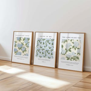 May include: Three framed prints with floral designs and inspirational quotes. The prints feature a white background with blue hydrangea flowers and green leaves. The quotes are "Steadfast Love", "Abide in Me", and "The Lord Bless You".