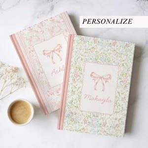 May include: Two personalized journals with floral and bow designs. One journal features a floral pattern, while the other has a lace-like design. Both have pink accents and the word "Personalize" is visible.