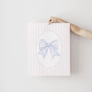 May include: A watercolor print of a blue bow with a floral pattern on a pink and white striped background.