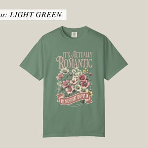 Pu&ograve; includere: T-shirt verde chiaro con la scritta "IT'S ACTUALLY ROMANTIC" sopra un disegno floreale. Il disegno comprende fiori rosa, bianchi e gialli. Sotto i fiori c'&egrave; uno striscione con la scritta "ALL THE EFFORT YOU PUT IN".