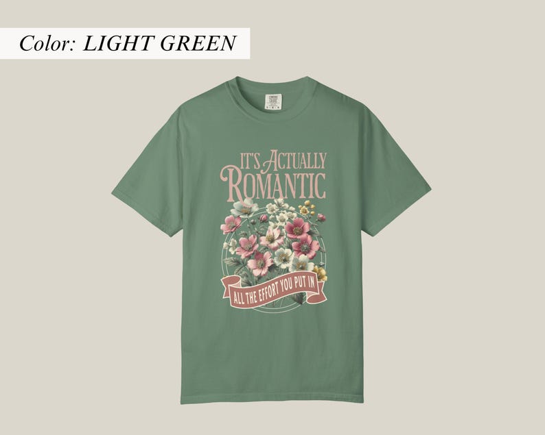 Pu&ograve; includere: T-shirt verde chiaro con la scritta "IT'S ACTUALLY ROMANTIC" sopra un disegno floreale. Il disegno comprende fiori rosa, bianchi e gialli. Sotto i fiori c'&egrave; uno striscione con la scritta "ALL THE EFFORT YOU PUT IN".