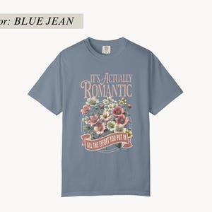 Pu&ograve; includere: T-shirt blu jeans con grafica floreale e la scritta "IT'S ACTUALLY ROMANTIC / ALL THE EFFORT YOU PUT IN". La grafica presenta fiori rosa, bianchi e gialli. La maglietta ha maniche corte e girocollo.