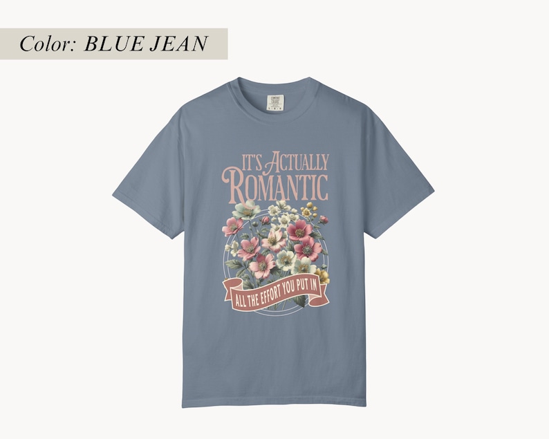 Pu&ograve; includere: T-shirt blu jeans con grafica floreale e la scritta "IT'S ACTUALLY ROMANTIC / ALL THE EFFORT YOU PUT IN". La grafica presenta fiori rosa, bianchi e gialli. La maglietta ha maniche corte e girocollo.