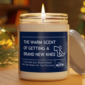 May include: A white candle in a glass jar with a blue label that reads "The warm scent of getting a brand new knee. A Get Well Soon Blend Infused with Well Wishes On Your Recovery. Salty Wit Candle Co. Vegan 9 oz."