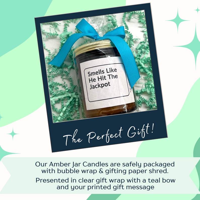 May include: A teal blue bow tied around a clear cellophane wrapped amber glass jar candle with a white label that reads "Smells Like He Hit The Jackpot". The candle is surrounded by green crinkle paper. The text "The Perfect Gift!" is written in black on a white background.