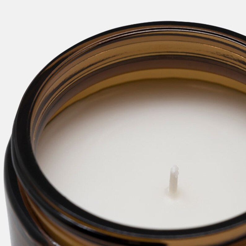 May include: A close-up of a white candle with a brown glass jar. The candle has a single wick.