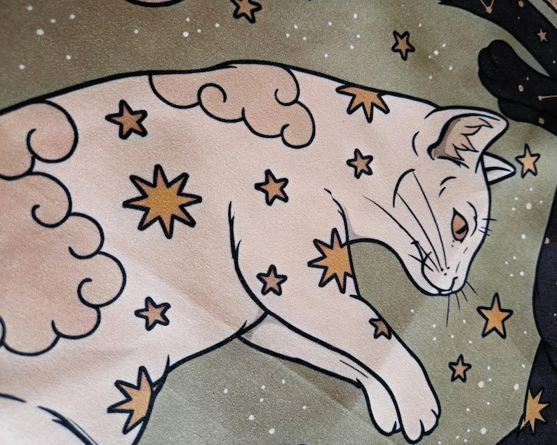 May include: A light beige cat illustration featuring gold star patterns and soft cloud shapes. The cat is depicted in a reclining position against a muted olive green background filled with small white dots and additional gold star motifs.