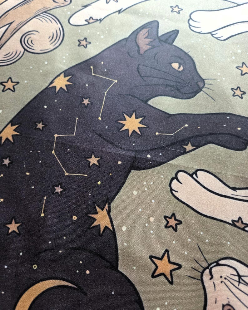 May include: A fabric print featuring a black cat adorned with gold stars and white constellation lines against a sage green background. The design includes stylized clouds and additional gold stars scattered across the surface of the material.
