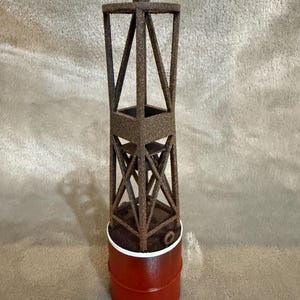 Op de afbeelding: Een decoratief boeimodel met een rode basis en een bruine, open framestructuur. De bovenkant van het model heeft een rood en bruin accent. De boei is ontworpen om op een nautische markering te lijken.