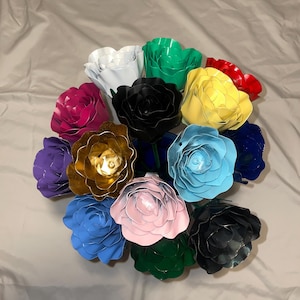 May include: A bouquet of 14 metal roses in various colors, including pink, blue, green, gold, white, black, purple, and red. The roses are arranged in a circular pattern.