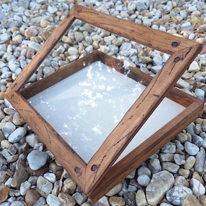 May include: A wooden display box with a hinged lid. The box is square with a clear glass top and a light-colored fabric interior. The wood has a natural finish with visible grain and is held together with small nails.