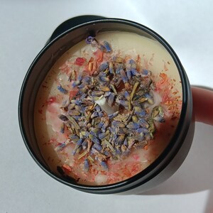 Pu&ograve; includere: Un barattolo di candela nero con una base di cera bianca e uno strato decorativo di lavanda secca e petali di fiori rosa.