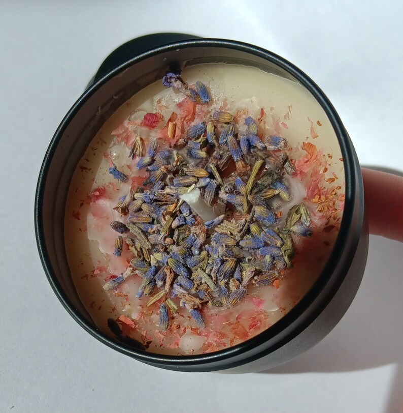 Pu&ograve; includere: Un barattolo di candela nero con una base di cera bianca e uno strato decorativo di lavanda secca e petali di fiori rosa.