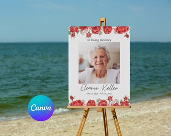 May include: A white memorial sign with a floral border of red roses. The sign has a photo of an older woman with gray hair and a white shirt. The text on the sign reads "In loving memory, Eleanor Keller, Dec 14, 1953 - Aug 25, 2023".