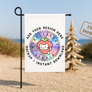 May include: A white garden flag on a black metal stand. The flag displays a colourful strawberry cat design with the text "ADD YOUR DESIGN HERE" and "MUDDLEBERRY STUDIO MOCKUP / INSTANT DOWNLOAD". The background is a beach scene.