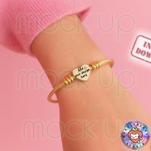 May include: Gold-colored bangle bracelet with a heart-shaped charm. The charm has the text "Add your design here". The bracelet is on a wrist against a pink background. The words "Instant Download" are in a red stamp.