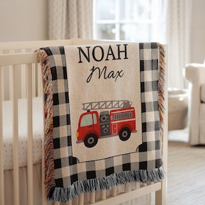 Può includere: Una coperta per bambini personalizzata con un design di camion dei pompieri rosso e i nomi "NOAH Max" in corsivo nero. La coperta presenta un motivo a quadri di bufalo in bianco e nero e frange.