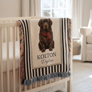 May include: A personalised baby blanket draped over a cot. The blanket features a brown dog wearing a red scarf, with the names "KOLTON" and "Dylan" printed below. The blanket has black and white striped edges and a fringed bottom.