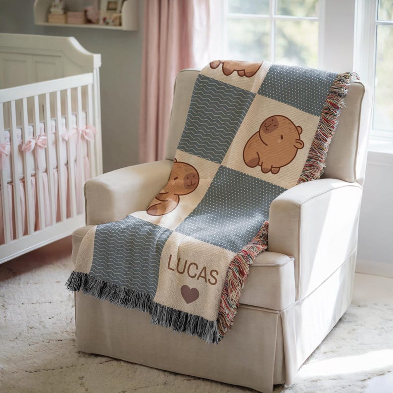 May include: A beige and blue patchwork baby blanket with a cartoon bear design. The blanket is draped over a white armchair in a nursery setting. The blanket has a fringe and the name "LUCAS" is displayed.