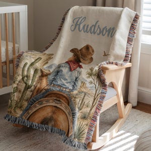 Cowboy baby blanket displayed as a warm western nursery accent with personalized baby name styling, rodeo horse details, and Southwest inspired charm. This custom baby blanket brings a sweet cowboy nursery look for baby boys, toddlers, and kids while fitting western baby gift ideas, baby boy quilt styling, first rodeo birthday décor, and horseback riding themes. A meaningful baby keepsake for families who love cowboy baby blankets and rodeo style.