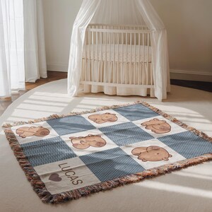 May include: A baby blanket with a patchwork design featuring light brown hippos on a blue and white background. The blanket has a fringed edge and the name "LUCAS" is printed on it, along with a heart symbol.