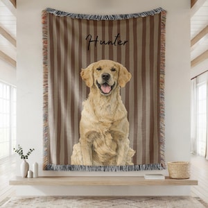 May include: A tan and brown striped tapestry with a smiling golden retriever dog illustration. The dog's name, "Hunter", is written in cursive above the dog. The tapestry has a fringed border and is hanging on a white wall.