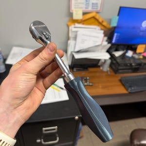 May include: A silver and black Pittsburgh brand ratchet wrench. The wrench has a black handle and a silver head. The handle is textured for grip. The wrench is a hand tool used for tightening or loosening bolts and nuts.