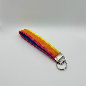 May include: A colorful key chain with a bright yellow, orange, and pink striped fabric strap and a silver key ring.