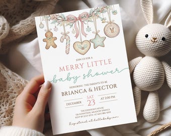 May include: A baby shower invitation with a festive design. The invitation features the text "Merry Little Baby Shower" and decorative gingerbread-themed ornaments. The invitation is held near a white stuffed bunny.