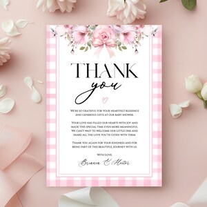 Puede incluir: Una tarjeta de agradecimiento para baby shower con un borde de cuadros rosas y detalles florales. La tarjeta presenta las palabras "THANK you" en una elegante escritura y letras en bloque, junto con un mensaje sincero.