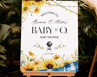 May include: A white baby shower sign on an easel, decorated with sunflowers and greenery. The sign reads "Welcome to Brianna & Hector's BABY Q BABY SHOWER" with a barbecue grill illustration and the date "JULY 25 2088".