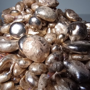May include: A close-up of a pile of irregularly shaped, metallic silver objects. The objects have a smooth, reflective surface with varying sizes and textures. The lighting creates highlights and shadows, enhancing the three-dimensional appearance of the objects.